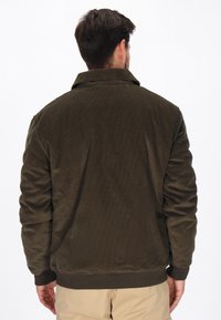 Sötét olíva zöld kordbársony dzseki. Nyakkal, bordázott mandzsettákkal és rugalmas derékkal rendelkezik. Az anyag textúrált, csíkos mintázatú.