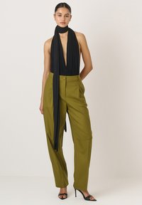 Juodas be rankovių viršus su giliu iškirpimu ir šalikėlio detale, derinamas su aukštu liemeniu alyvinių žalių kelnių. Juodi aukštakulniai sandalai baigia įvaizdį.