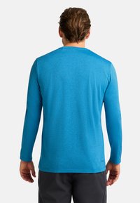 Maglietta a maniche lunghe di un brillante colore blu, realizzata in un materiale traspirante con una finitura texturizzata. Presenta un collo rotondo e un design minimalista.