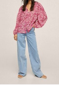 Blusa rosa con estampado floral y mangas abullonadas, escote en forma de V, combinada con jeans de pierna ancha en un tono azul claro y sandalias beige. Textura de tela suave.
