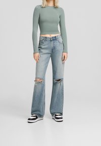 Light green long-sleeve cropped top, paired with light blue wide-leg jeans featuring rips at the knees and black and white sneakers.