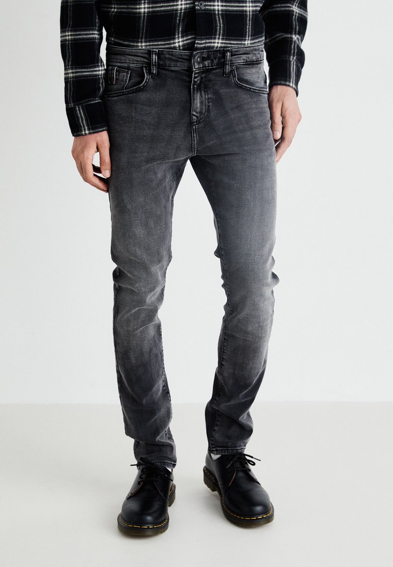 Chemise à carreaux noir et gris à manches longues, assortie à un jean noir délavé et des chaussures noires avec des coutures jaunes.