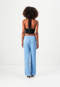Haut halter noir court avec un lien à l'arrière, associé à un pantalon large plissé bleu clair avec des rayures verticales et des talons coordonnés.