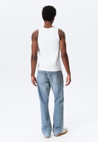 White tank top and light blue denim jeans, featuring a relaxed fit. Smooth texture, basic design, and visible stitching details.
