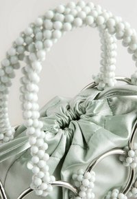 Sac à poignée perlée avec un corps en satin doux vert clair. Présente une quincaillerie circulaire argentée et une fermeture supérieure froncée.