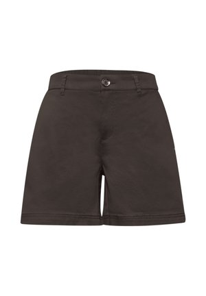 Zbliżenie kieszeni ciemno-brązowych spodni z metalową metką marki powyżej, noszone z wsuniętą czarno-białą pasiastą koszulą.