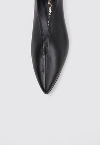 Chaussure noire en cuir à bout pointu avec un design épuré, présentant une couture au centre et une texture lisse. Profil plat, style minimaliste.