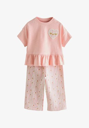 Rózsaszín rövid ujjú felső fodros szegéllyel és szív alakú folttal, fehér nadrággal párosítva, amelyen rózsaszín csíkok és apró virágminták találhatók.