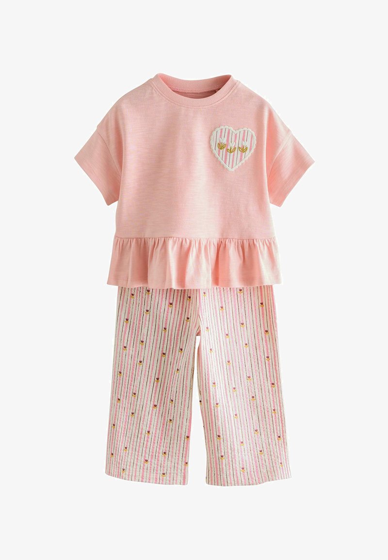 Haut rose à manches courtes avec ourlet volanté et écusson en forme de cœur, associé à un pantalon blanc orné de rayures roses et de petits motifs floraux.