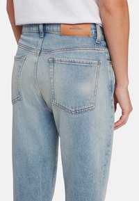 Jeans in denim azzurro chiaro con vita alta, gamba dritta e cuciture a contrasto. Presenta un'etichetta in pelle e due tasche posteriori.
