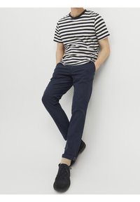 Randig kortärmad t-shirt i marinblått och krämfärgat, kombinerad med marinblå byxor. Skorna är svarta med en strukturerad yta. Neutral bakgrund.