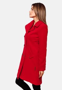 Roter Mantel mit tailliertem Schnitt, großem Kragen und Knopfverschluss. Verfügt über seitliche Taschen und kontrastierende Hardware-Akzente. Glatte Textur.