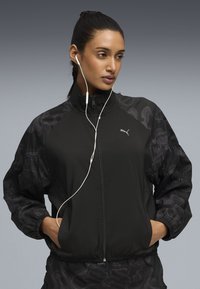 Μαύρο μπουφάν με φερμουάρ και μοτίβο στα μανίκια. Διαθέτει ψηλό γιακά, ελαστικά μανσέτες και ακουστικά. Κατασκευασμένο από ελαφρύ, απαλό υλικό.