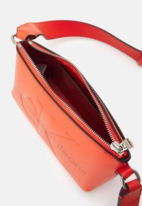Borsa in ecopelle rossa con logo Calvin Klein Jeans in rilievo, zip argentata e tracolla regolabile. Interno con slot per schede.