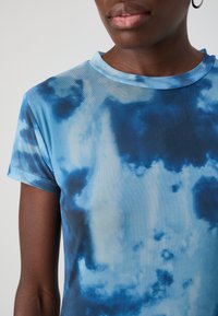 Modrá tričko s krátkym rukávom v štýle tie-dye, so zaobleným výstrihom, hladkou textúrou a postupným farebným prechodom od svetlo do tmavo modrej.