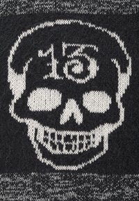 Černá pletenina má bílé design kostry s kruhovým obrysem a dekorativními prvky. Textura je měkká a vzorovaná.