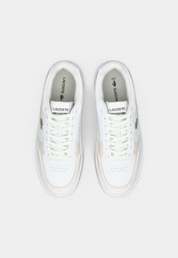 Λευκά αθλητικά παπούτσια από δέρμα και σουέτ, με τρυπητές λεπτομέρειες, υφασματικές αποχρώσεις και κλείσιμο με κορδόνια. Ορατό λογότυπο Lacoste.
