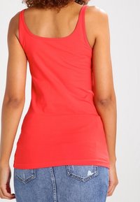 Top rosso senza maniche con design aderente realizzato in tessuto elasticizzato. La parte posteriore presenta una texture liscia e una scollatura arrotondata.