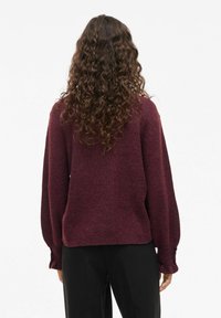 Maglione a maglia borgogna con una vestibilità comoda, spalle scese e polsini a coste. Texture morbida, peso medio e silhouette casual.