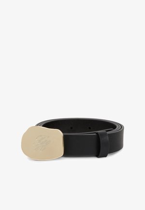 Ceinture en cuir noir roulée avec une boucle en or irrégulière gravée d’initiales en écriture cursive sur fond blanc.