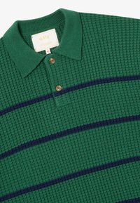 Polo vert en maille avec deux boutons bruns et des rayures horizontales bleu marine, montrant un col côtes et un tissu texturé.