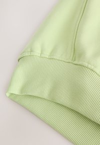 Sudadera verde claro con una tela superior lisa y puños acanalados. La textura parece suave, con detalles sutiles de costura.