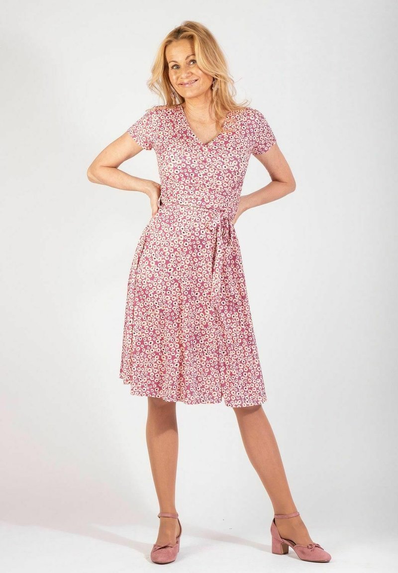 Kukallinen kietaisumekko vaaleanpunaisesta kankaasta, lyhythihaisilla hihoilla, polvipituisella helmalla ja nauhavyötäröllä. Kuosissa on pieniä valkoisia kukkia.