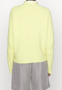 Hellgelber, flauschiger Pullover mit rundem Ausschnitt und geripptem Saum, kombiniert mit braunen und weißen gestreiften Shorts.