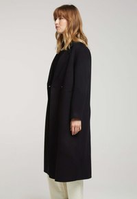 Manteau noir long au design structuré, avec un col cranté et des poches latérales. Texture douce, manches longues et silhouette droite.