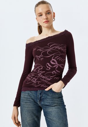 Bordowy top z długim rękawem i odsłoniętymi ramionami, z koronkowym wykończeniem oraz stylizowanym nadrukiem tekstowym w jaśniejszych odcieniach fioletu.
