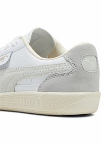 Vita lädersneaker med grå mockadetaljer, gummisula, texturerad mellansula och framträdande logotypdetalj på sidan och hälen.