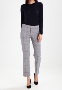 Marinblå långärmad topp och grå rutiga byxor med rak passform och en polerad finish. Svarta högklackade skor fulländar outfiten.