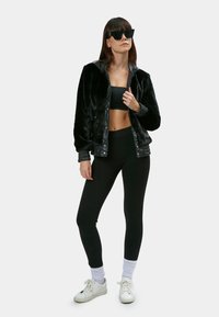 Sort faux fur bomberjakke med læderdetaljer, parret med en sort crop top og leggings. Hvide sneakers med teksturerede detaljer.