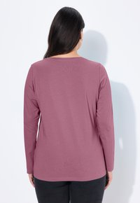 Dlouhý rukáv top v mušelínové barvě, s kulatým výstřihem a jemným materiálem. Zadní strana má minimální švy a běžný střih.