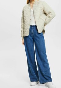 Chaqueta bomber acolchada de color beige claro con un patrón de rombos, combinada con jeans de tiro alto y pierna ancha de color azul y zapatillas blancas.