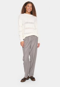 Cream knitted sweater with lace-like horizontal stripes, paired with light gray pleated trousers and brown shoes with tassel accents.