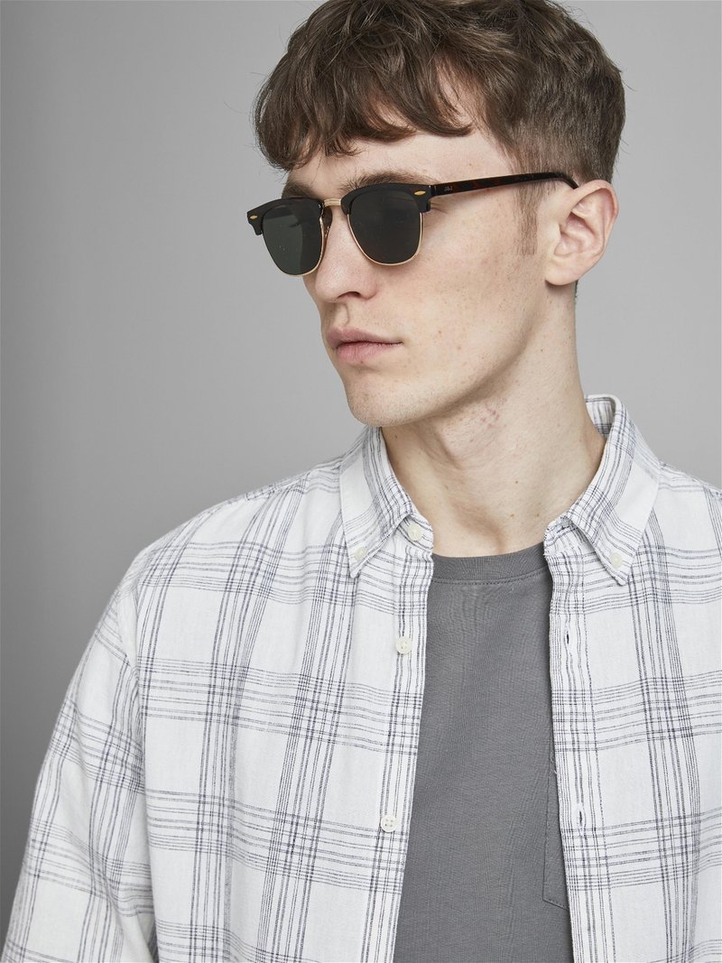 Ochelari de soare cu lentile negre într-o ramă cu model țestoasă. Modelul poartă un tricou gri sub o cămașă albă cu carouri.