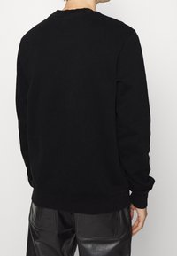 Svart sweatshirt med rund hals och långa ärmar. Tygblandning av bomull, ribbade ärmslut och nedre kant, minimalistisk design utan synliga mönster.