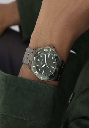 Orologio al quarzo con quadrante verde scuro e cinturino in acciaio inossidabile argentato. Presenta indici luminosi, lunetta girevole e display della data alle 3.