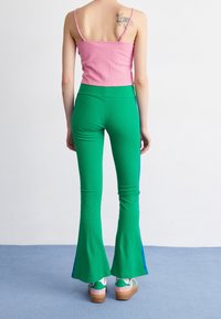 Rosa ribbad kort tanktopp i kombination med gröna utsvängda byxor med blå sidosträck, bärs med flerfärgade platåskor.