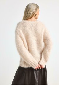 Maglione leggero rosa chiaro, morbido e fluffy, con vestibilità ampia, spalle basse e polsini ripiegati, indossato sopra una gonna di pelle nera.