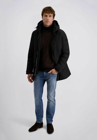 Zwarte geïsoleerde jack met een capuchon, ritssluiting aan de voorkant en drukknopen; gedragen over een donker sweater en gecombineerd met blauwe jeans en donkere enkellaarsjes.