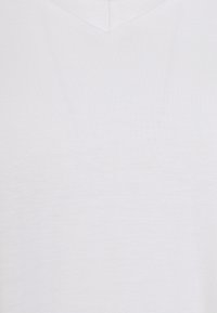 Bílá V-čková košile, textura látky zblízka, se zaměřením na jemný pletený vzor a hladký povrch.