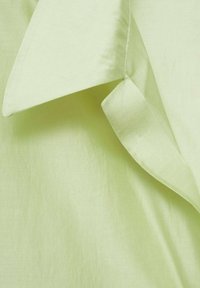 Gros plan d'un col et d'un revers de chemise vert pâle montrant un tissu lisse et des détails de couture.