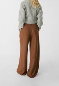 Hnědé široké kalhoty vyrobené z hladkého materiálu s dobře střiženým designem. Obsahují zadní kapsy a vysoký pas. Spárovaný šedý zkrácený svetr.
