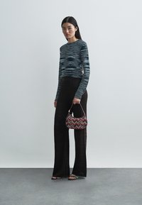 Hosszú fekete csíkos nadrág, testhez simuló csíkos felső, és egy kis mintás kézitáska piros és fehér részletekkel. Sima textúrák és összhangban lévő dizájn.