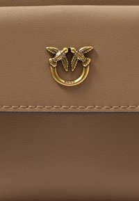 Beige leather bag featuring a gold-tone metal clasp shaped like two birds, with fine stitching along the edges and a smooth texture.