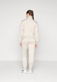Lys grå hettejakke med ribbede mansjetter, kombinert med matchende tapered bukser. Antrekket er laget av et glatt stoff, med en avslappet passform.