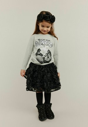 Gray long-sleeve shirt with "DISCO" graphic, paired with a black layered flower skirt, black tights, and embellished black boots.