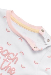 Prenda de bebé de tela blanca con patrones de arcoíris en tonos pasteles, ribete rosa y detalles amarillos. Cuenta con botones a presión en el hombro para facilitar el cambio de ropa.